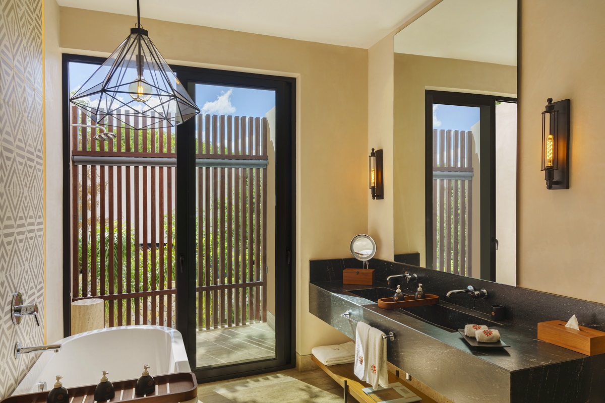 Elegant bathroom with freestanding tub and black countertop; lush views through wooden slats at Hacienda Xcanatun, Angsana Heritage Collection.
